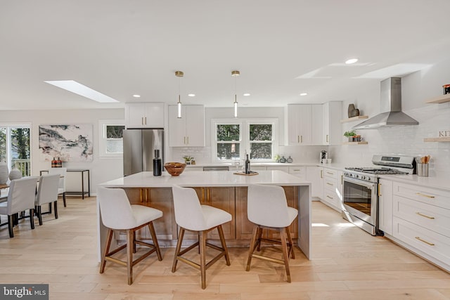 kitchen with wall chimney range hood, hanging light fixtures, white cabinets, and appliances with stainless steel finishes