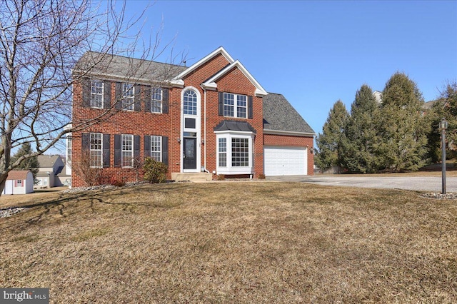 colonial house featuring driveway, an attached garage, a front yard, and brick siding