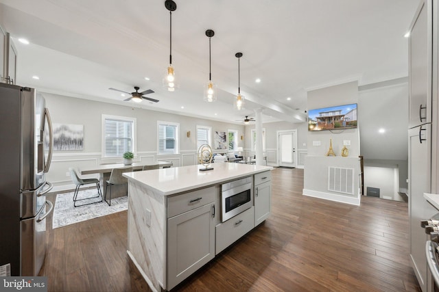 kitchen with dark wood-type flooring, crown molding, decorative light fixtures, appliances with stainless steel finishes, and a kitchen island