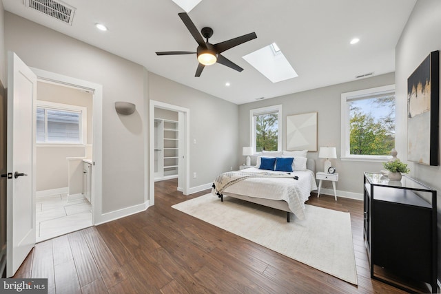 bedroom with ensuite bath, a walk in closet, a skylight, dark hardwood / wood-style flooring, and ceiling fan