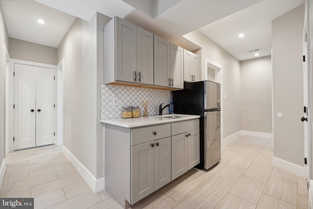 kitchen featuring gray cabinets, tasteful backsplash, sink, and stainless steel refrigerator