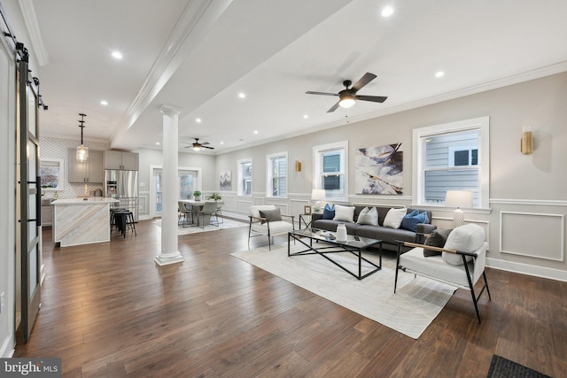 living room with ornate columns, ornamental molding, a barn door, and ceiling fan