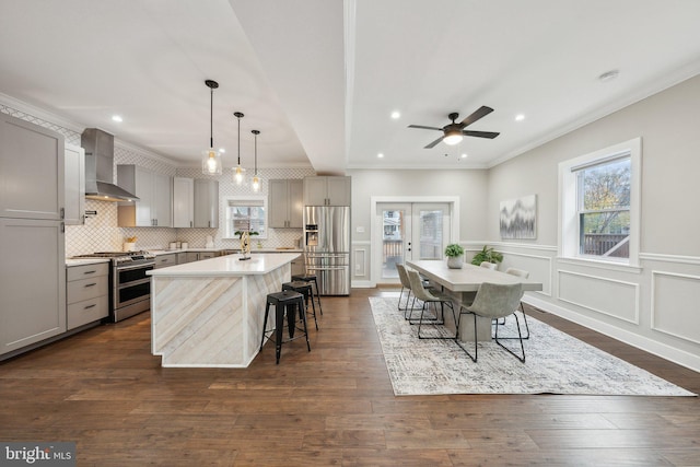 kitchen with pendant lighting, gray cabinetry, a kitchen island with sink, stainless steel appliances, and wall chimney exhaust hood