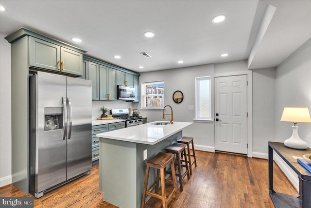 kitchen with sink, a breakfast bar area, dark hardwood / wood-style flooring, a kitchen island with sink, and stainless steel appliances