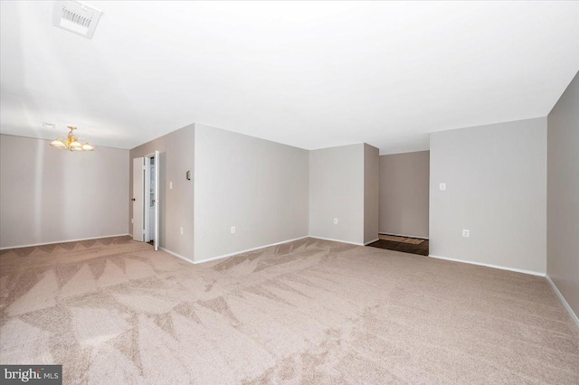 empty room featuring light colored carpet and a notable chandelier