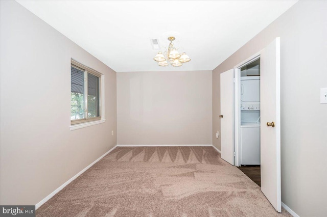 carpeted spare room with stacked washer / drying machine and an inviting chandelier