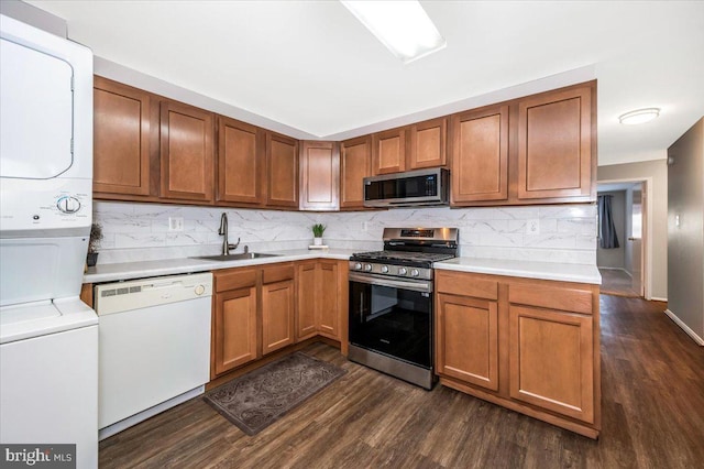 kitchen featuring dark hardwood / wood-style flooring, stainless steel appliances, sink, backsplash, and stacked washer and clothes dryer