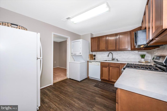 kitchen featuring white appliances, decorative backsplash, sink, dark hardwood / wood-style floors, and stacked washer and clothes dryer