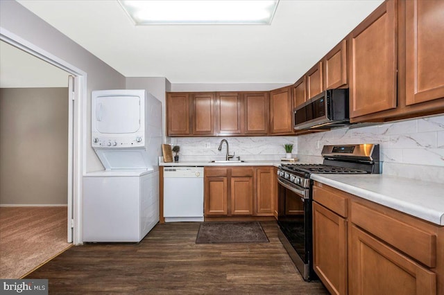 kitchen featuring dark hardwood / wood-style flooring, sink, appliances with stainless steel finishes, tasteful backsplash, and stacked washer / dryer