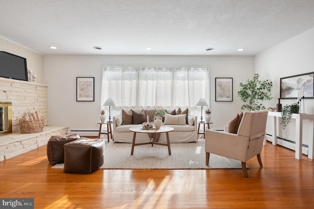 living room featuring a baseboard radiator, a fireplace, a textured ceiling, and light wood-type flooring