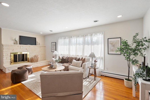 living room featuring a baseboard radiator, a stone fireplace, and light hardwood / wood-style flooring