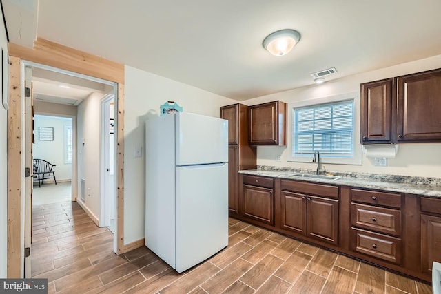 kitchen with light stone counters, sink, and white refrigerator