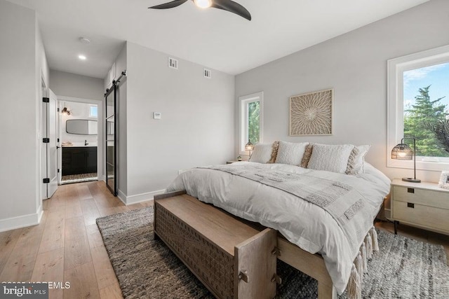 bedroom featuring ceiling fan, light hardwood / wood-style flooring, ensuite bath, and a barn door