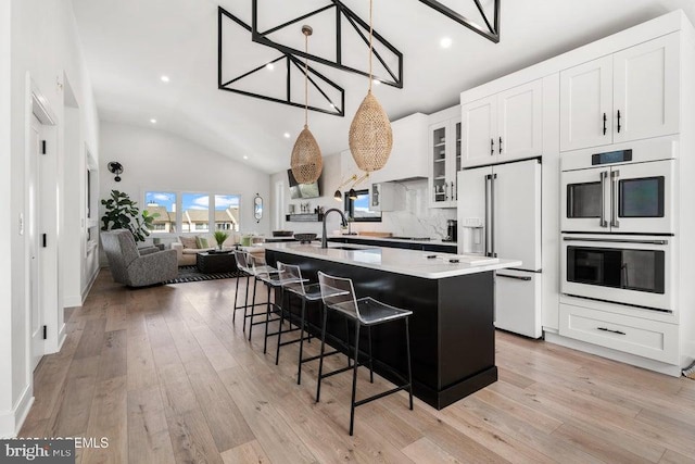 kitchen featuring sink, white cabinets, white appliances, a center island with sink, and a breakfast bar area