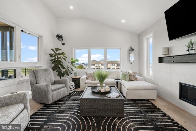 living room featuring hardwood / wood-style floors, lofted ceiling, and a tiled fireplace