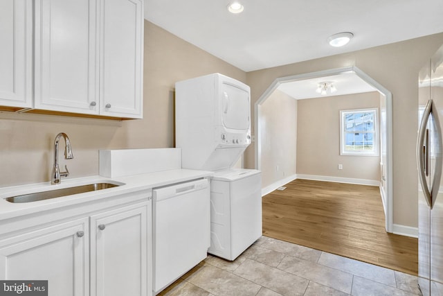 laundry area with sink, light tile patterned floors, and stacked washer and dryer