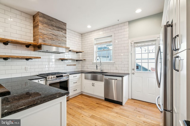 kitchen featuring sink, white cabinetry, light wood-type flooring, stainless steel appliances, and wall chimney range hood