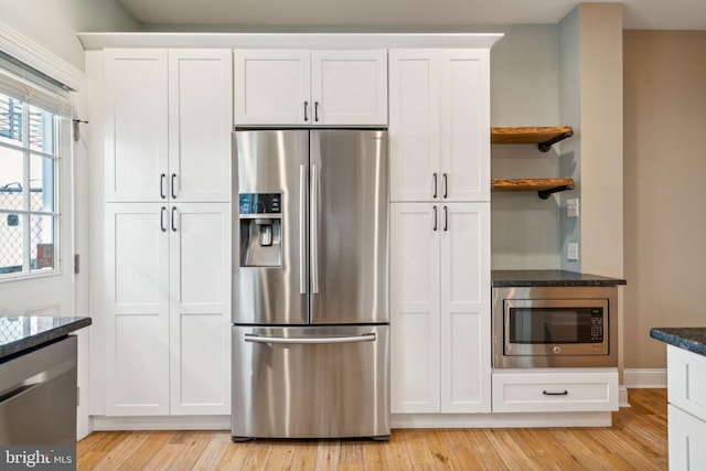 kitchen with white cabinetry, stainless steel appliances, dark stone counters, and light wood-type flooring