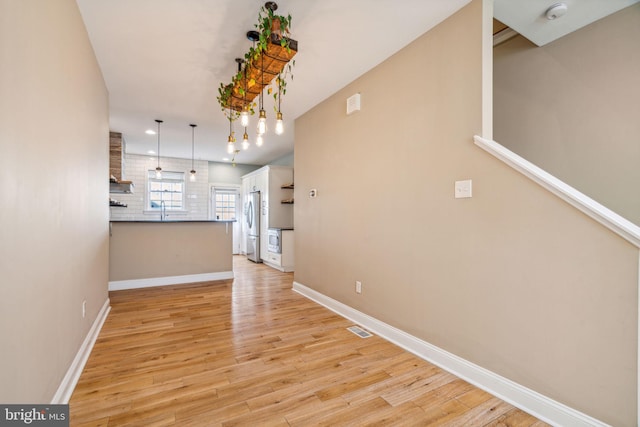 interior space featuring stainless steel refrigerator, sink, white cabinets, hanging light fixtures, and light wood-type flooring