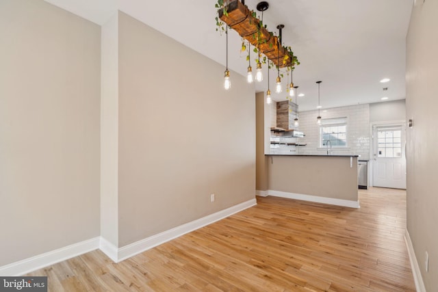 interior space with sink, backsplash, light hardwood / wood-style floors, kitchen peninsula, and wall chimney range hood