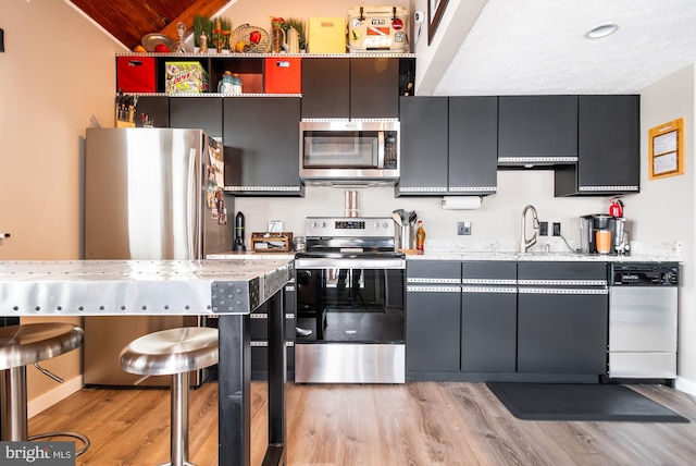 kitchen with stainless steel appliances, light stone countertops, sink, and light wood-type flooring