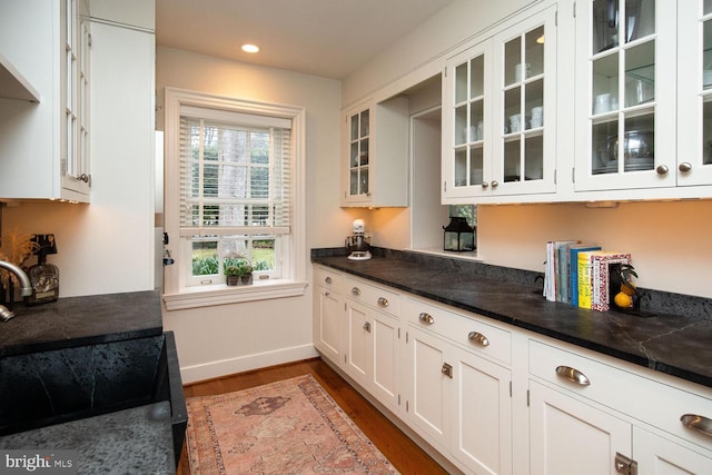 kitchen with wall chimney exhaust hood, sink, dark hardwood / wood-style floors, dark stone counters, and white cabinets