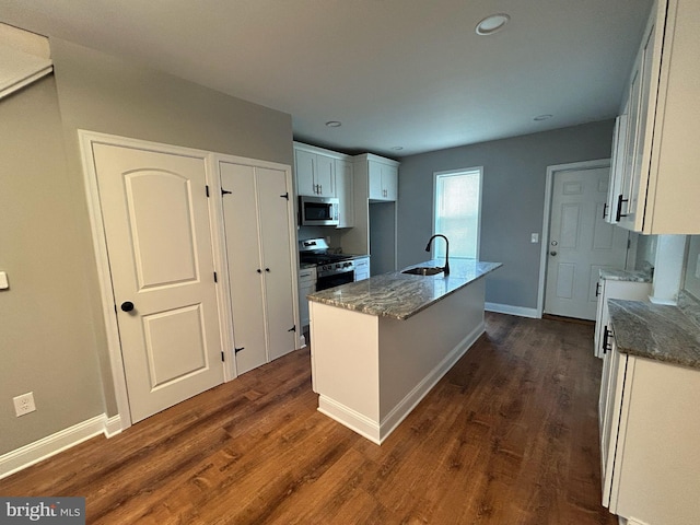 kitchen featuring appliances with stainless steel finishes, white cabinetry, dark stone countertops, sink, and a kitchen island with sink