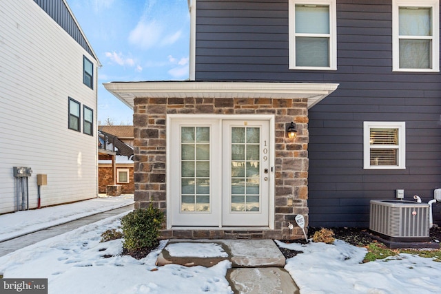 snow covered property entrance featuring central AC and french doors