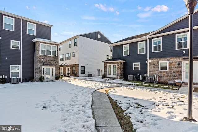 snow covered property with central AC unit and french doors