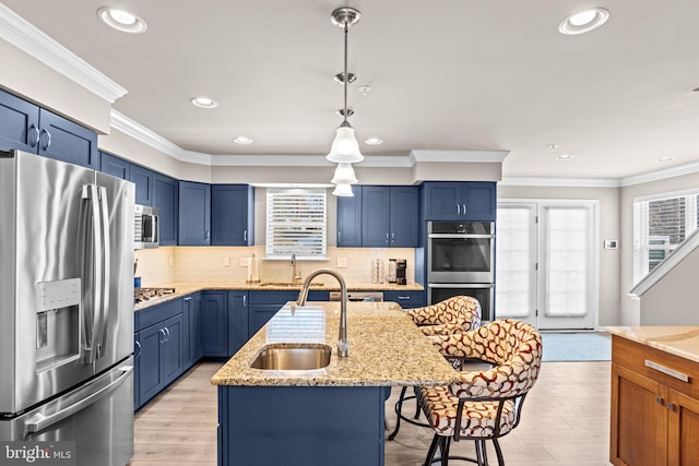 kitchen featuring sink, appliances with stainless steel finishes, light stone countertops, an island with sink, and decorative light fixtures