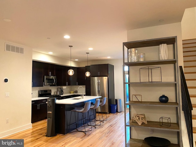 kitchen with appliances with stainless steel finishes, decorative light fixtures, backsplash, a center island with sink, and a breakfast bar area