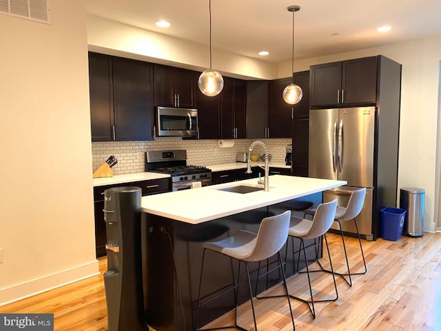 kitchen featuring sink, stainless steel appliances, light hardwood / wood-style floors, and pendant lighting