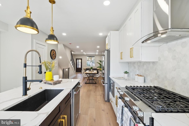 kitchen with sink, white cabinetry, light stone countertops, and wall chimney range hood