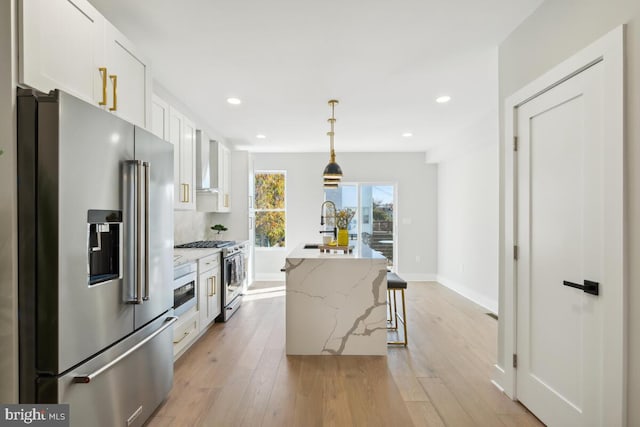 kitchen featuring pendant lighting, appliances with stainless steel finishes, white cabinetry, an island with sink, and light stone counters