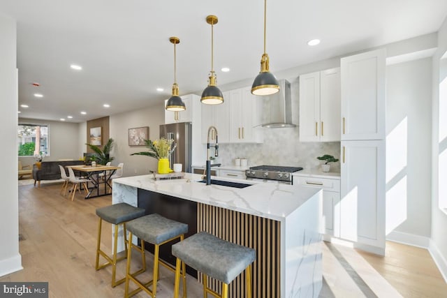 kitchen with tasteful backsplash, white cabinets, decorative light fixtures, an island with sink, and wall chimney exhaust hood