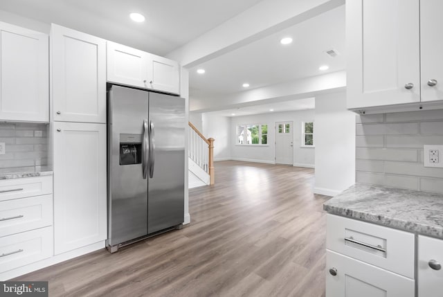 kitchen with light stone countertops, stainless steel fridge with ice dispenser, decorative backsplash, and white cabinets