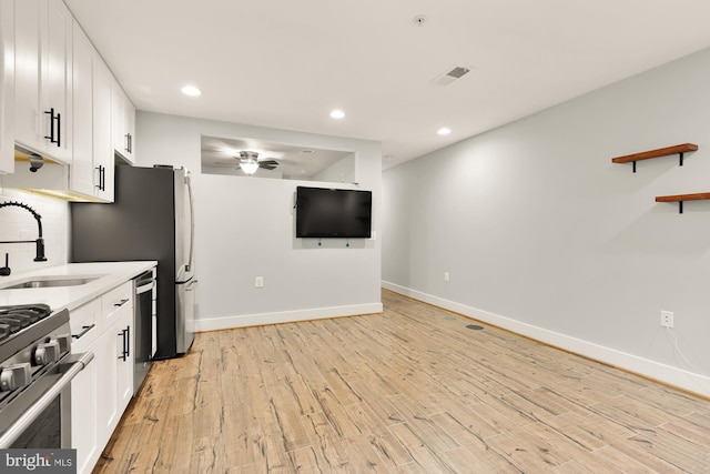 kitchen featuring white cabinets, stainless steel appliances, decorative backsplash, sink, and light wood-type flooring