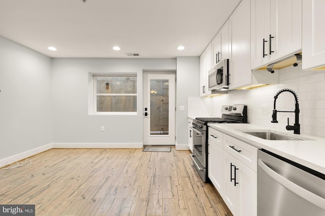 kitchen with sink, white cabinetry, stainless steel appliances, and light wood-type flooring