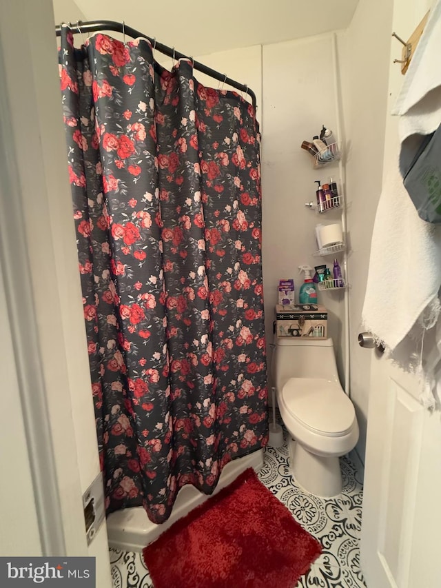 bathroom featuring toilet, curtained shower, and tile patterned flooring