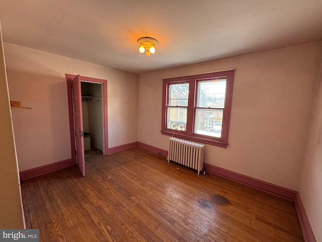 unfurnished bedroom with wood-type flooring, radiator heating unit, and a closet