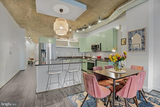 kitchen featuring hardwood / wood-style flooring, green cabinetry, decorative backsplash, sink, and stainless steel appliances