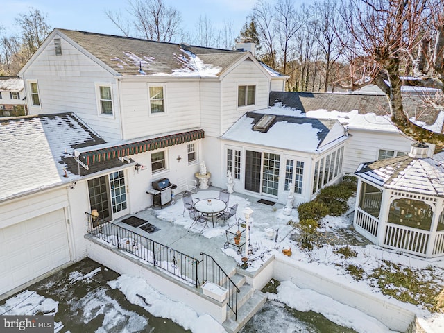 snow covered rear of property with a garage and a sunroom