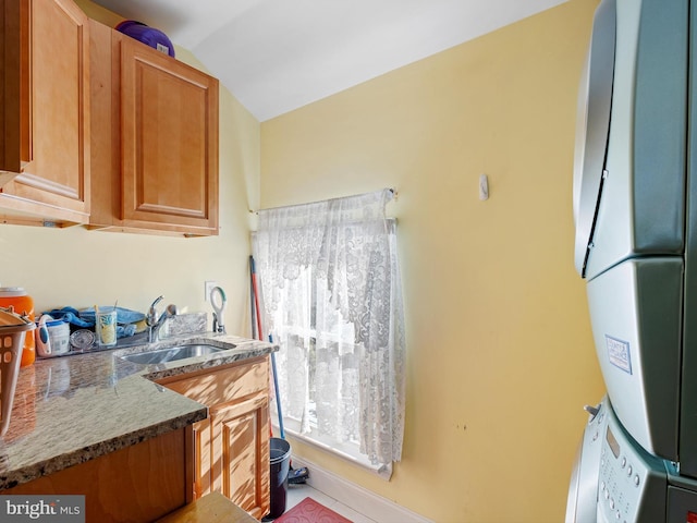 kitchen featuring lofted ceiling, stacked washer / dryer, sink, and dark stone countertops