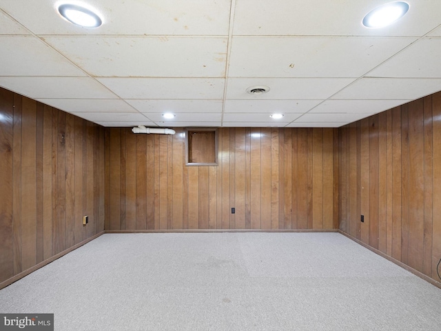 basement featuring a paneled ceiling, light colored carpet, and wooden walls