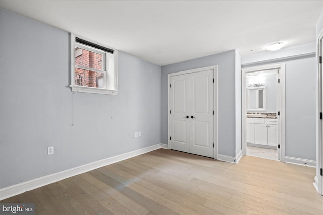 unfurnished bedroom with a closet, ensuite bathroom, and light hardwood / wood-style flooring