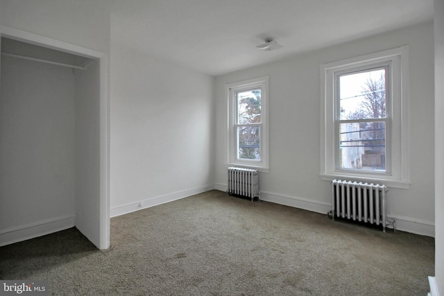 unfurnished bedroom with radiator heating unit, multiple windows, and carpet