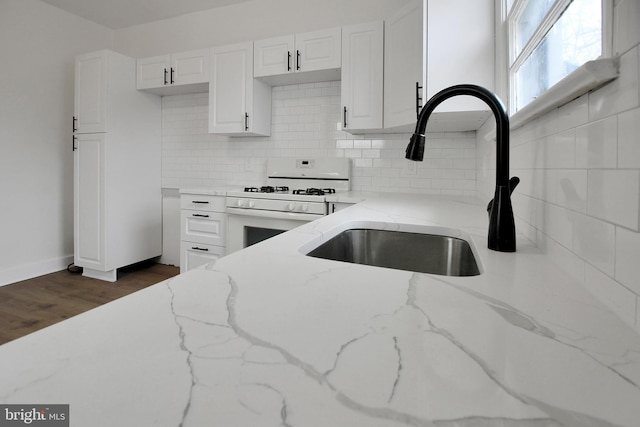 kitchen with white cabinets, sink, dark hardwood / wood-style flooring, white gas range, and light stone counters