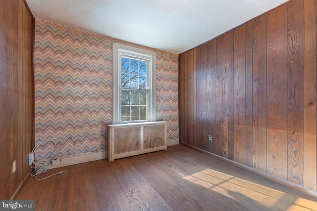 empty room featuring hardwood / wood-style flooring, radiator, and wooden walls