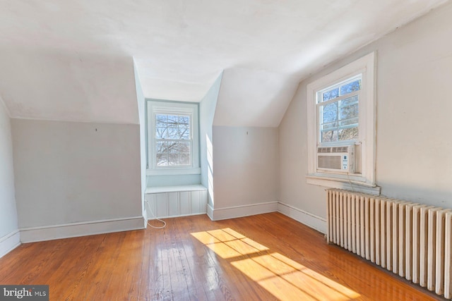 additional living space featuring vaulted ceiling, plenty of natural light, radiator, hardwood / wood-style floors, and cooling unit