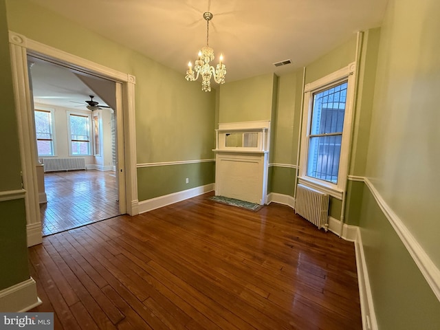 unfurnished dining area featuring ceiling fan with notable chandelier, dark hardwood / wood-style floors, and radiator heating unit